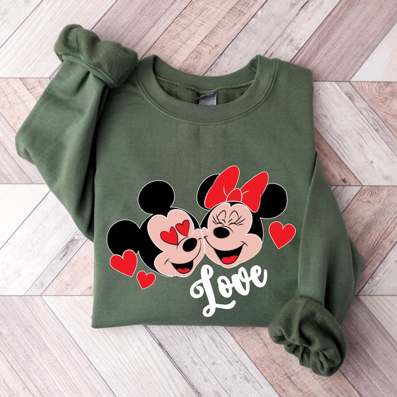 May include: Green sweatshirt with a graphic of Mickey Mouse and Minnie Mouse kissing. The graphic is in red and white with the word "Love" underneath.