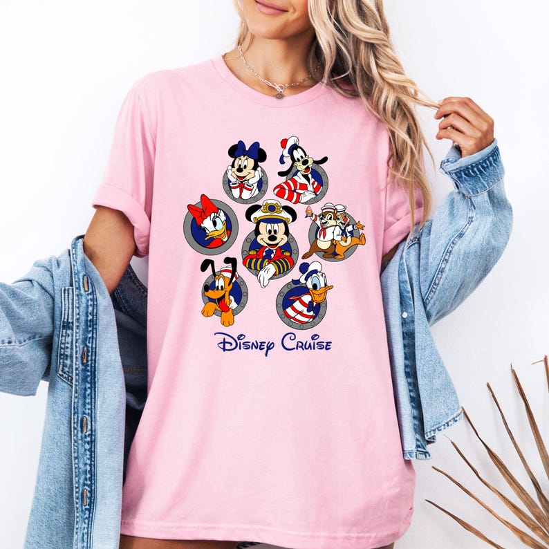 May include: Pink t-shirt featuring Disney characters in circular frames. Characters include Mickey Mouse, Minnie Mouse, Donald Duck, Daisy Duck, Goofy, Pluto, and Chip and Dale. The text "Disney Cruise" is printed in blue script below the characters.