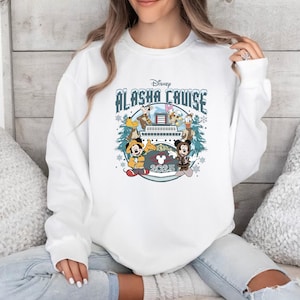 Pu&ograve; includere: Felpa girocollo bianca con un design Disney Alaska Cruise. Il design include Topolino e Minnie, Paperino e Pippo, con il testo "Alaska Cruise 2025" in una grafica a tema invernale.