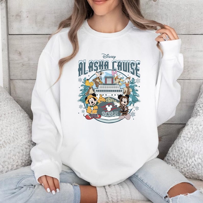 Pu&ograve; includere: Felpa girocollo bianca con un design Disney Alaska Cruise. Il design include Topolino e Minnie, Paperino e Pippo, con il testo "Alaska Cruise 2025" in una grafica a tema invernale.