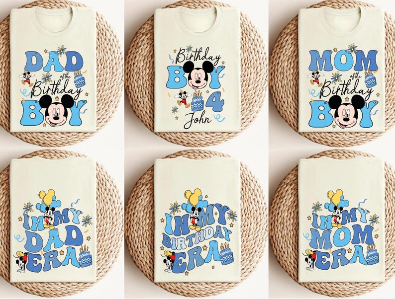 Op de afbeelding: Cr&egrave;mekleurige T-shirts met blauwe tekst en Mickey Mouse-afbeeldingen. Ontwerpen zijn onder meer "Dad of the Birthday Boy", "Birthday Boy 4 John", "Mom of the Birthday Boy", en "In My Dad Era", "In My Birthday Era", en "In My Mom Era."