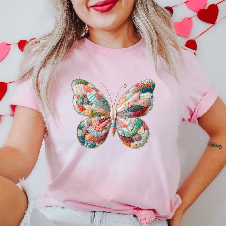 May include: A light pink t-shirt featuring a colorful butterfly design. The butterfly is made of various fabric patches in shades of pink, green, blue, and yellow. The shirt has short sleeves and a round neckline.