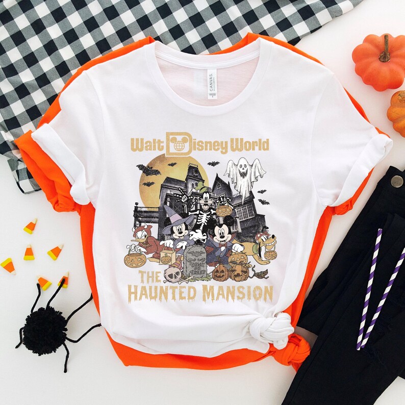 May include: White t-shirt with a graphic of Mickey Mouse and friends in front of the Haunted Mansion at Walt Disney World. The text "Walt Disney World" and "The Haunted Mansion" are printed on the shirt.