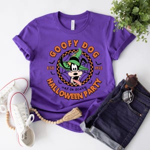 May include: Purple t-shirt featuring a graphic of Goofy dressed as a ghost. The graphic reads "Goofy Dog Est. 1932 Halloween Party not so scary".
