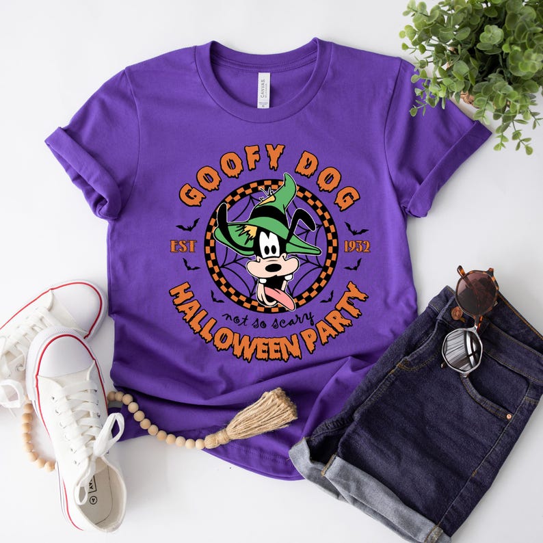 May include: Purple t-shirt featuring a graphic of Goofy dressed as a ghost. The graphic reads "Goofy Dog Est. 1932 Halloween Party not so scary".