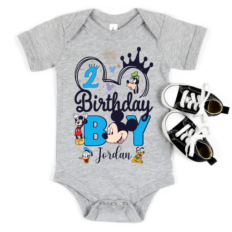 Op de afbeelding: Een grijs rompertje met een blauw en zwart Mickey Mouse ontwerp. Het ontwerp bevat een kroon, vuurwerk en de tekst "2 Birthday Boy Jordan".