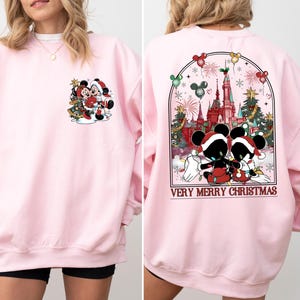 May include: Pink sweatshirt with a Christmas-themed design featuring Mickey Mouse and Minnie Mouse in front of a Christmas tree. The back of the sweatshirt has a design of Mickey Mouse and Minnie Mouse in front of a castle with the text "Very Merry Christmas".