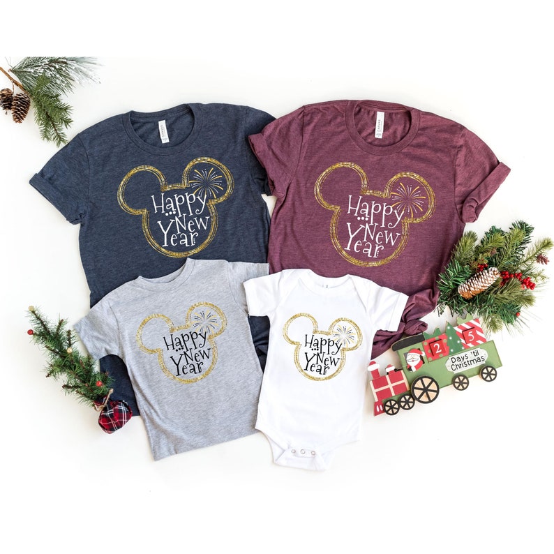 May include: A set of four t-shirts featuring a gold glitter Mickey Mouse head with the text "Happy New Year" inside. The shirts are in navy blue, burgundy, grey, and white.