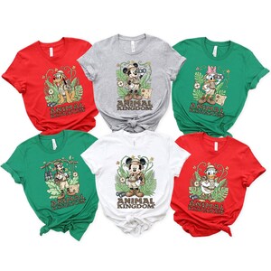 May include: A collection of six t-shirts in various colors: red, gray, green, and white. Each shirt features a different Disney character in safari attire with the words "Animal Kingdom" printed below the character.