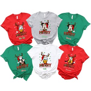 May include: A collection of Christmas-themed t-shirts in red, gray, green, and white. Each shirt features a Disney character wearing a Santa hat and reindeer antlers, with the words "Merry Christmas" and a family role printed below.
