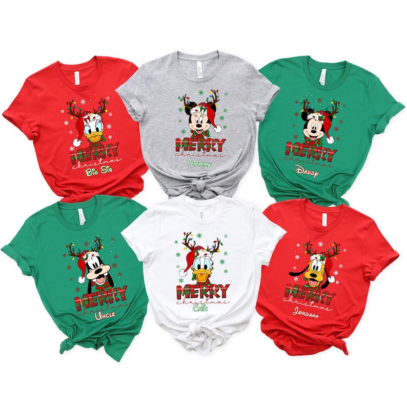 May include: A collection of Christmas-themed t-shirts in red, gray, green, and white. Each shirt features a Disney character wearing a Santa hat and reindeer antlers, with the words "Merry Christmas" and a family role printed below.