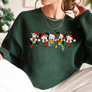 May include: Green Christmas sweater with a line of cartoon characters wearing Santa hats. The characters include Mickey Mouse, Donald Duck, Goofy, and Pluto.