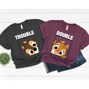 May include: Two t-shirts with a cartoon chipmunk peeking out of a frame. The gray shirt says "Trouble" and the maroon shirt says "Double".