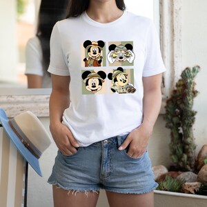 K&ouml;nnte beinhalten: Wei&szlig;es T-Shirt mit vier Panels, die Micky Maus in Safari-Kleidung zeigen. Jedes Panel zeigt eine andere Pose von Micky, der einen Safarihut und -outfit tr&auml;gt, mit Fernglas und Kamera. Der Hintergrund ist eine Mischung aus Gr&uuml;n, Beige und Oliv.