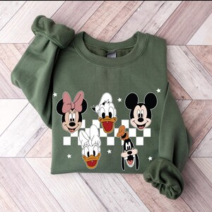 Puede incluir: Sudadera verde con un patr&oacute;n a cuadros e im&aacute;genes de dibujos animados de Mickey Mouse, Minnie Mouse, Donald Duck, Daisy Duck y Goofy.