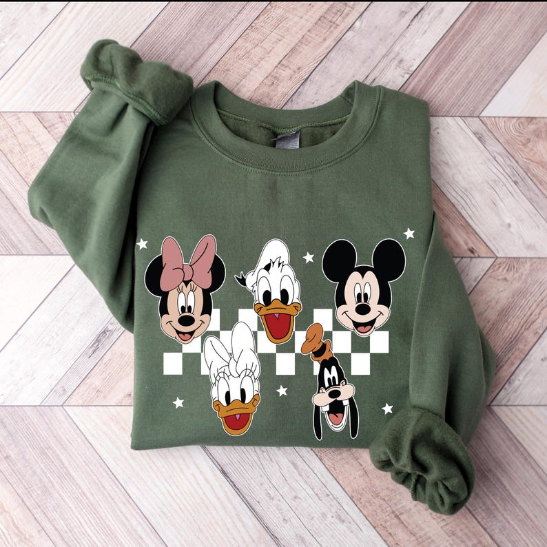 Puede incluir: Sudadera verde con un patr&oacute;n a cuadros e im&aacute;genes de dibujos animados de Mickey Mouse, Minnie Mouse, Donald Duck, Daisy Duck y Goofy.