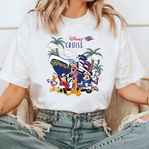 Pu&ograve; includere: Maglietta bianca con una grafica colorata di Topolino, Minnie Mouse, Paperino, Pippo e Pluto in piedi davanti a una nave da crociera Disney. Il testo "Disney Cruise" &egrave; stampato sopra i personaggi.