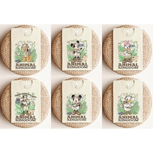May include: Six cream-colored t-shirts featuring Disney characters in safari outfits. Each shirt has a different character: Pluto, Mickey Mouse, Daisy Duck, Goofy, and Donald Duck. The text "ANIMAL KINGDOM" is printed at the bottom of each shirt.