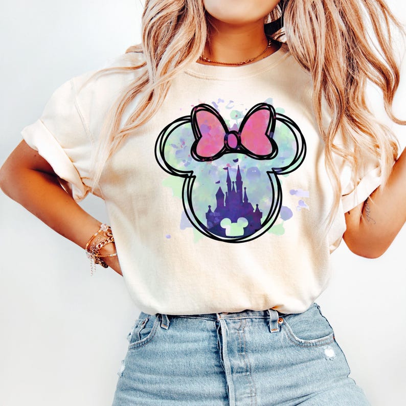 May include: A white t-shirt with a watercolor design of a Mickey Mouse head with a pink bow. Inside the head is a silhouette of Cinderella's castle.