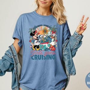 May include: Blue jean-colored t-shirt featuring a colorful graphic of Minnie Mouse and Daisy Duck on a cruise ship. The text "Girls gone CRUISING" is printed below the graphic. The shirt has short sleeves.