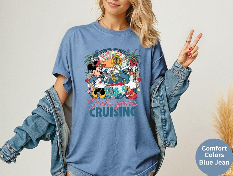 May include: Blue jean-colored t-shirt featuring a colorful graphic of Minnie Mouse and Daisy Duck on a cruise ship. The text "Girls gone CRUISING" is printed below the graphic. The shirt has short sleeves.
