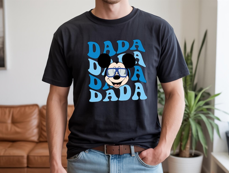 K&ouml;nnte beinhalten: Schwarzes T-Shirt mit einem blauen Retro-Design, das dreimal das Wort "DADA" zeigt. In der Mitte befindet sich eine Cartoon-Mickey-Mouse mit Brille. Dieses l&auml;ssige T-Shirt ist ein Alltagsartikel.