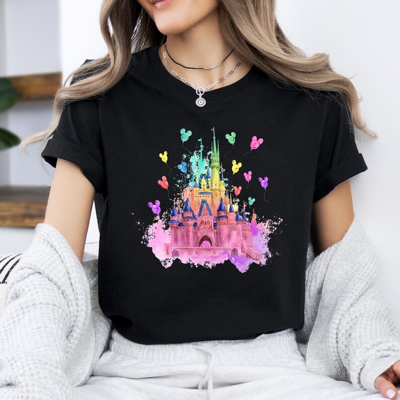 May include: Black t-shirt with a rainbow watercolor illustration of Cinderella's castle with Mickey Mouse ears floating around it.