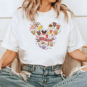 May include: White t-shirt with a Mickey Mouse head design made of various Disney park food and treats. The text "Best Day Ever" is on a red ribbon.