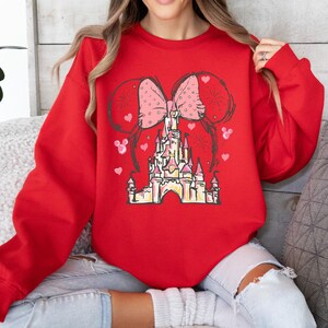 May include: Red sweatshirt with a pink bow and a cartoon drawing of Cinderella's castle.