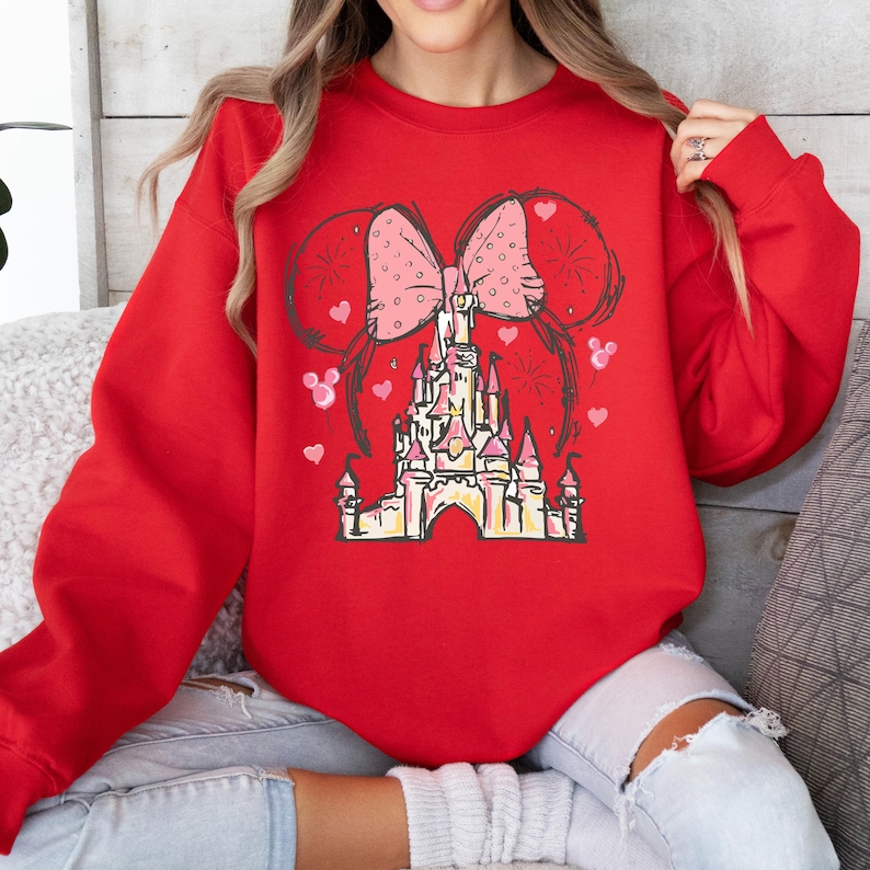 May include: Red sweatshirt with a pink bow and a cartoon drawing of Cinderella's castle.
