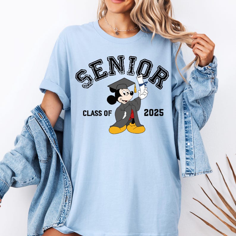 K&ouml;nnte beinhalten: Hellblaues T-Shirt mit einer schwarzen Grafik von Mickey Mouse, der einen Abschluss-Hut tr&auml;gt und ein Diplom h&auml;lt. Der Text "Senior Class of 2025" ist auf dem Shirt aufgedruckt.