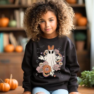 May include: Black sweatshirt with a white ghost wearing a bow and surrounded by flowers and stars. The ghost has a surprised expression and is holding its arms out. The text "Boo!" is printed on the sweatshirt.