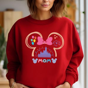May include: Red sweatshirt with a graphic of Mickey Mouse ears, a bow, a castle, and the word "MOM" in a colorful design.