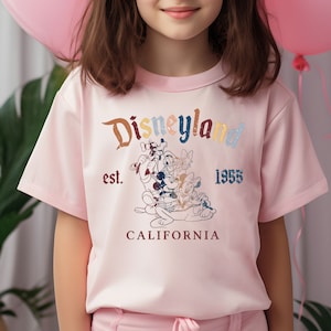 May include: Pink short-sleeved t-shirt with a vintage-style graphic of Mickey Mouse and friends in front of the Disneyland logo. The text reads "Disneyland est. 1955 CALIFORNIA".