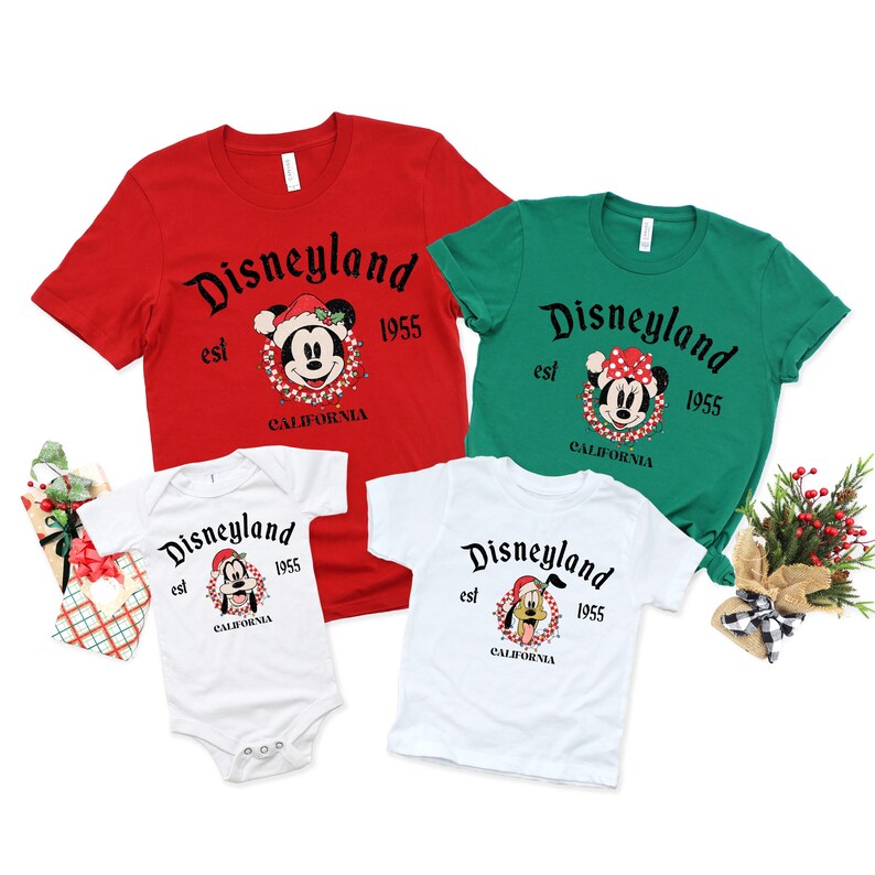 May include: A set of four t-shirts featuring a Christmas-themed Disneyland logo with Mickey Mouse and Pluto. The shirts are red, green, and white. The text on the shirts reads "Disneyland est 1955 California".