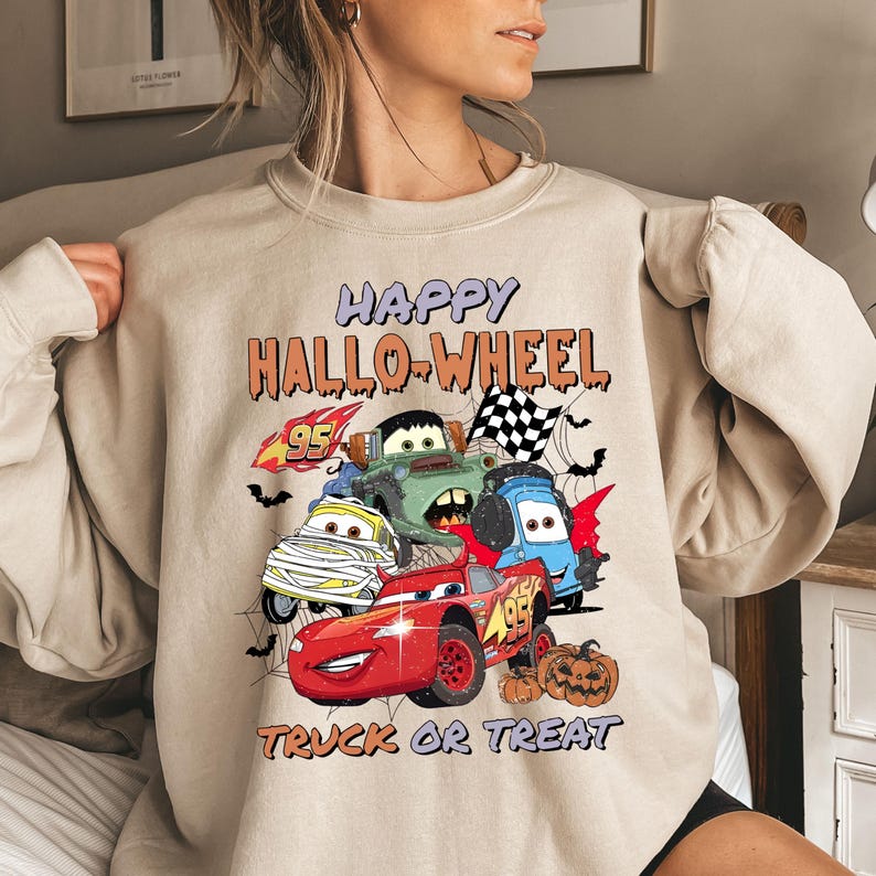 May include: A beige sweatshirt with a graphic print of cartoon cars and the text "Happy Hallo-Wheel Truck or Treat".