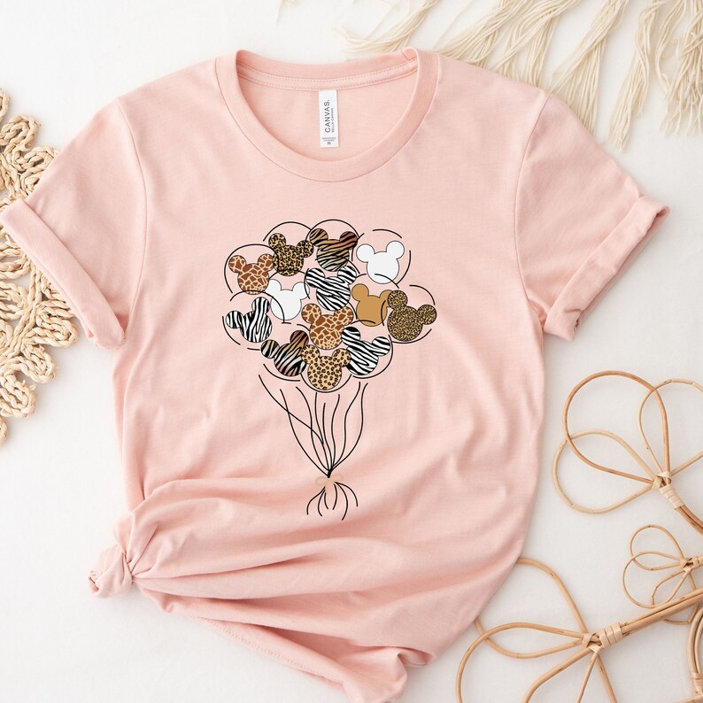 Puede incluir: Una camiseta rosa con un gr&aacute;fico de un mont&oacute;n de cabezas de Mickey Mouse con forma de globos. Los globos est&aacute;n impresos con diferentes estampados de animales, incluyendo cebra, leopardo y guepardo.
