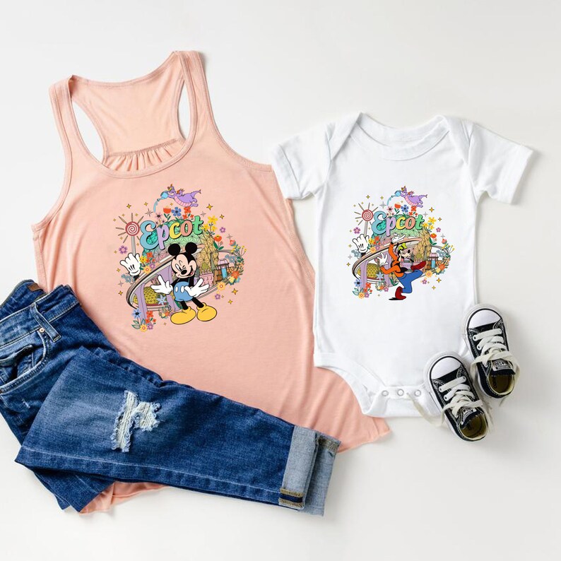 May include: A pink tank top and a white bodysuit with a colorful graphic of Mickey Mouse and Goofy at Epcot. The graphic features a roller coaster, flowers, and the Epcot logo.