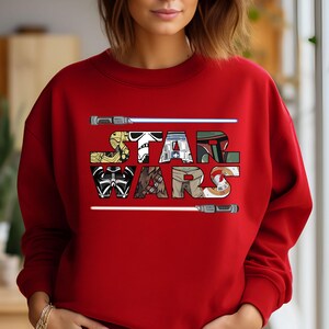 May include: Red sweatshirt with a white graphic of the Star Wars logo. The logo is made up of different Star Wars characters, including Darth Vader, Yoda, and R2-D2.