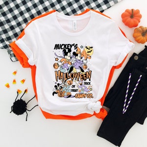 May include: White t-shirt with a graphic of Mickey Mouse and friends dressed in Halloween costumes. The text on the shirt reads "Mickey's Halloween or Treat Candy Co."