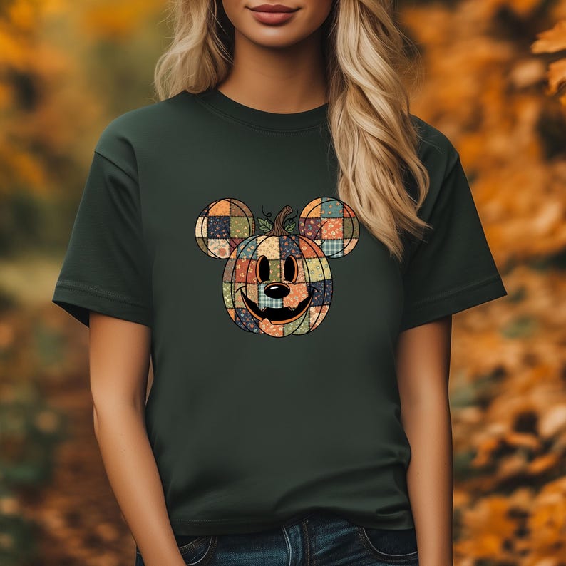 May include: Dark green t-shirt featuring a patchwork pumpkin design with Mickey Mouse ears. The pumpkin has a smiling face and is made of various colorful squares. The shirt is a short-sleeved crew neck.