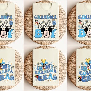 K&ouml;nnte beinhalten: Sechs wei&szlig;e T-Shirts mit blauen und gelben Designs, die Mickey Mouse und den Text "Grandpa of the Birthday Boy", "Grandma of the Birthday Boy", "Cousin of the Birthday Boy", "In My Grandpa Era", "In My Grandma Era" und "In My Cousin Era" zeigen.