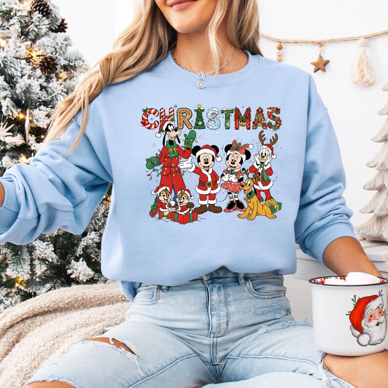 May include: Light blue Christmas sweatshirt featuring a graphic of Disney characters, including Mickey and Minnie Mouse, Goofy, Pluto, and Chip and Dale. The word "CHRISTMAS" is displayed across the top in a festive font. The sweatshirt has long sleeves.