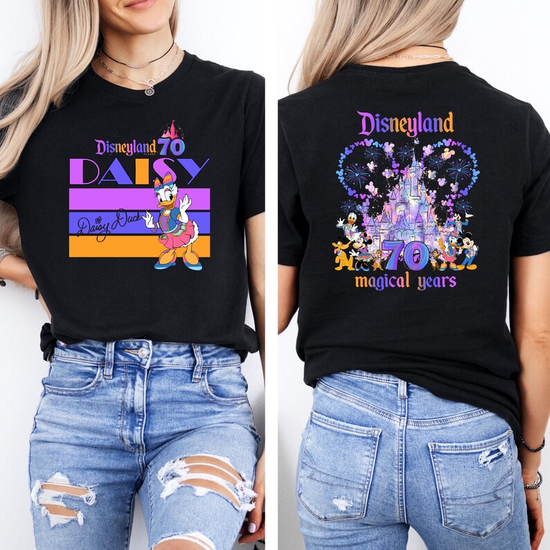 May include: Two black t-shirts with a Disneyland 70th anniversary theme. The front shirt features Daisy Duck with the text "Disneyland 70 Daisy" and "Daisy Duck" in a signature. The back shirt features a purple and blue illustration of Sleeping Beauty's castle with fireworks and the text "Disneyland 70 magical years".
