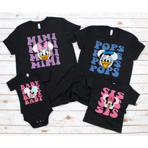 Puede incluir: Camisetas negras y un body con personajes de Disney. Las camisetas tienen las palabras "MIMI", "POPS", "BABY" y "SIS" con gr&aacute;ficos de personajes. El body tiene un gr&aacute;fico de beb&eacute; Minnie Mouse. Las camisetas son de manga corta.