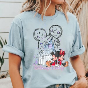 May include: Pale blue t-shirt with a Disney Family design. The graphic features Mickey and Minnie Mouse, a castle, fireworks, and the words "Disney Family". The design uses black, red, purple, and white colours.