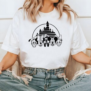 May include: White t-shirt with a black graphic of Mickey Mouse, Minnie Mouse, Donald Duck, Goofy, and Pluto in front of the iconic Cinderella's Castle.