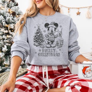 May include: A gray sweatshirt with a black and white graphic of Mickey Mouse in a Santa hat, holding a drink, and standing next to a Christmas tree. The text "MERRY CHRISTMAS" is below the graphic. The person is wearing red and white plaid pajama pants.
