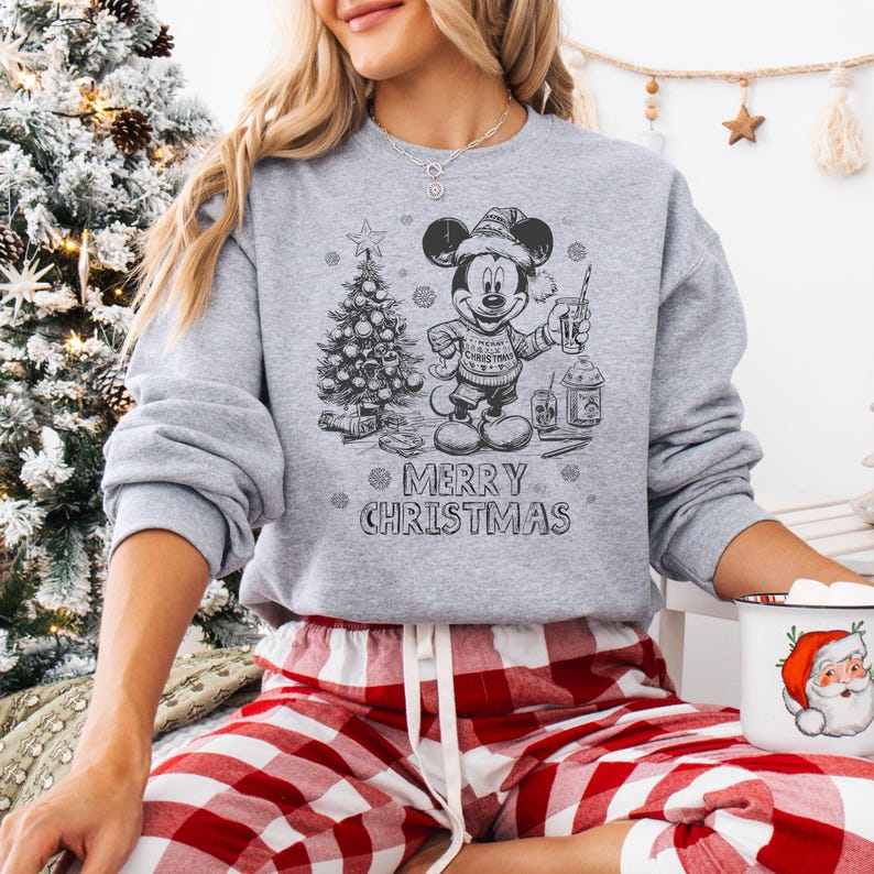 May include: A gray sweatshirt with a black and white graphic of Mickey Mouse in a Santa hat, holding a drink, and standing next to a Christmas tree. The text "MERRY CHRISTMAS" is below the graphic. The person is wearing red and white plaid pajama pants.