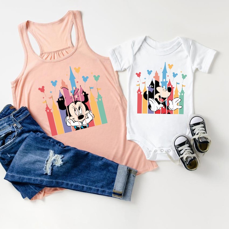 May include: A pink tank top and a white bodysuit with a colorful graphic of Mickey Mouse and Minnie Mouse in front of a castle with balloons.